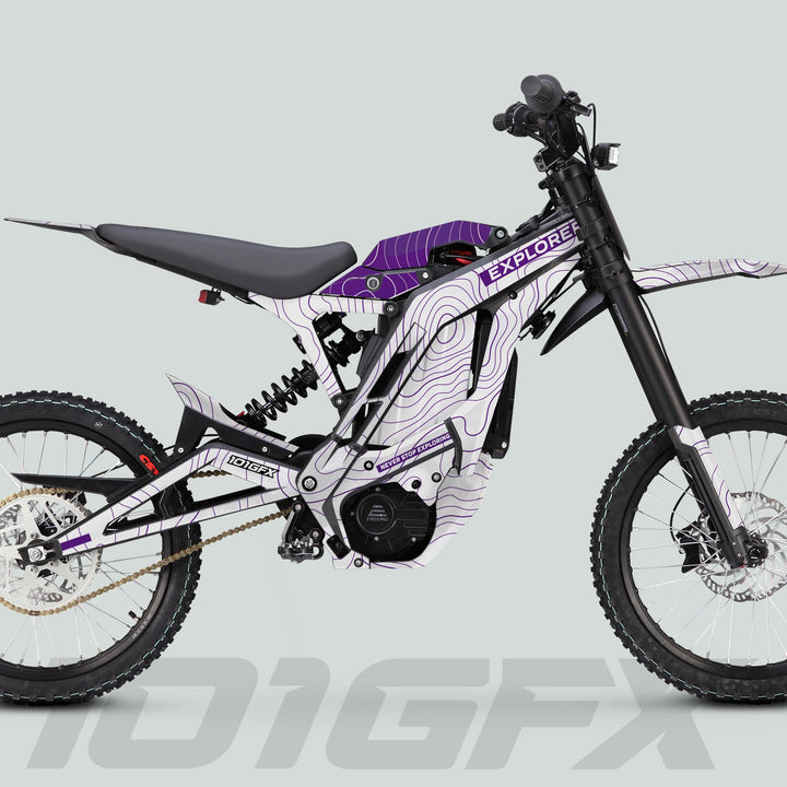 Side-view of E Ride Pro SS Graphics Kit EXPLORER White Purple on an off-road e-dirt bike with high-rise handlebar, coil shock, and knobby tires.