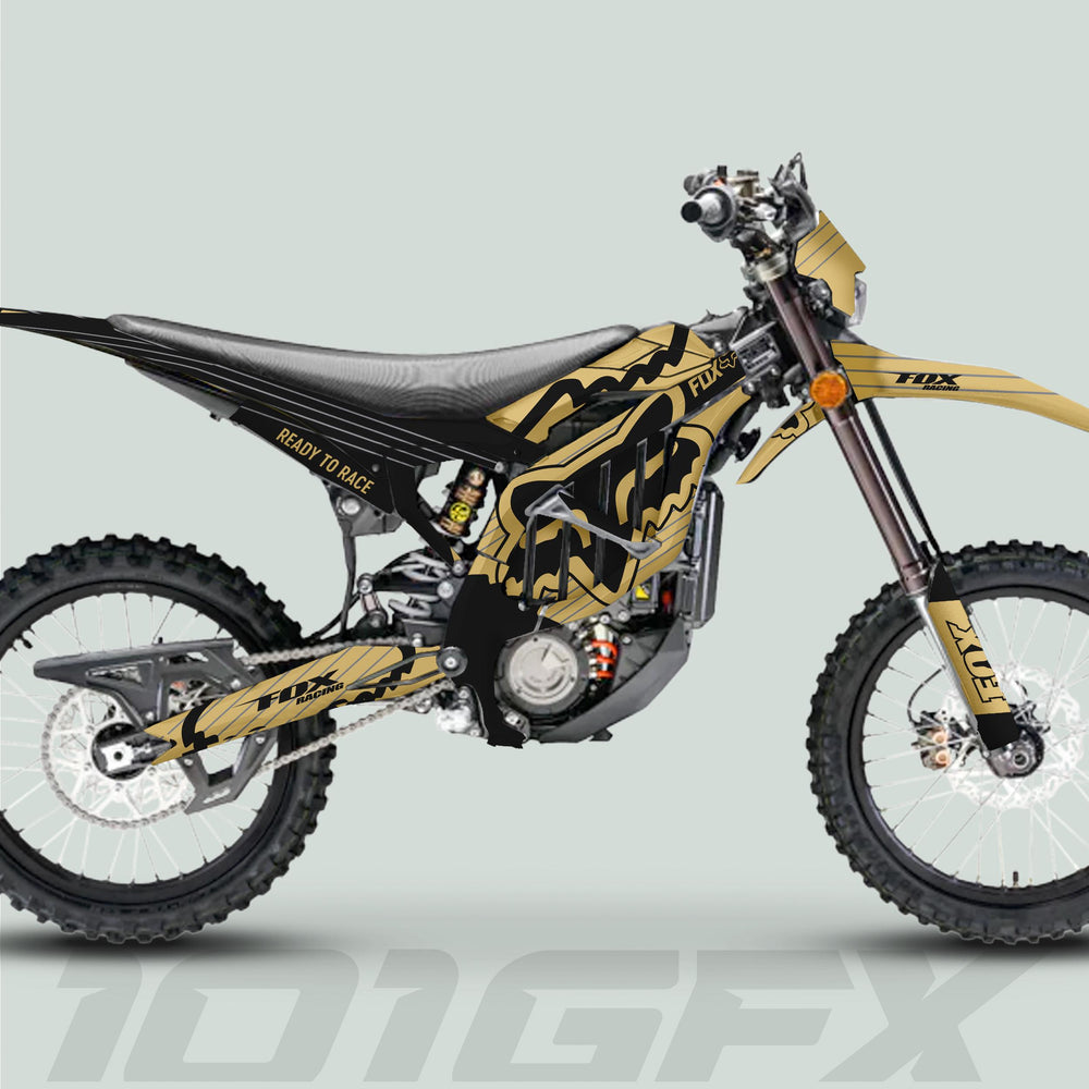 Surron Ultra Bee Graphics Kit FOX STRIPES Sand Black on a motocross bike, featuring gold-black Fox decals, ribbed seat, Fox-branded swingarm, and knobby tires.