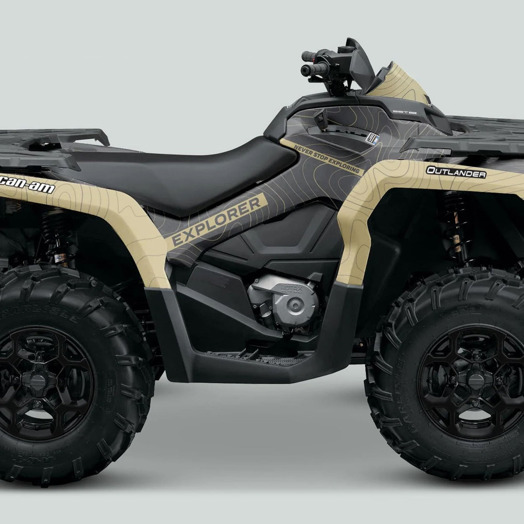 Side view of a Can-Am OUTLANDER G2 Graphics Kit EXPLORER Grey Sand on an ATV, showcasing its rugged design, chunky tires, and protective graphics.