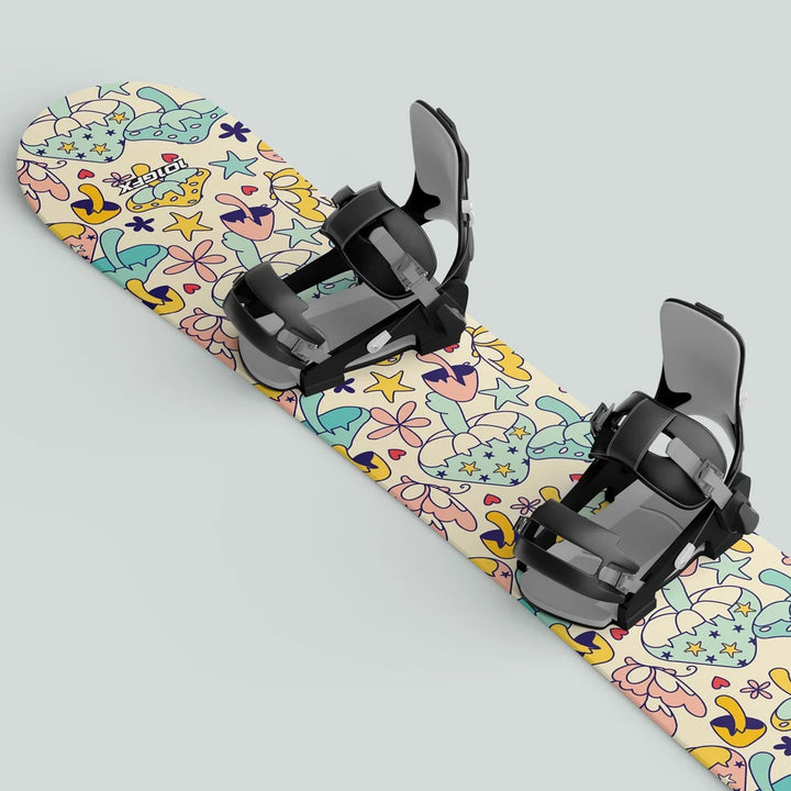 Snowboard with MAGIC MUSHROOMS wrap, featuring pastel patterns of stars, flowers, and mushrooms, equipped with adjustable black bindings for a unique ride.