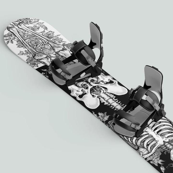 Snowboard with black strap-in bindings featuring Snowboard Wrap RIDER FOREVER WHITE, showing a skull and floral design for protection and customization.