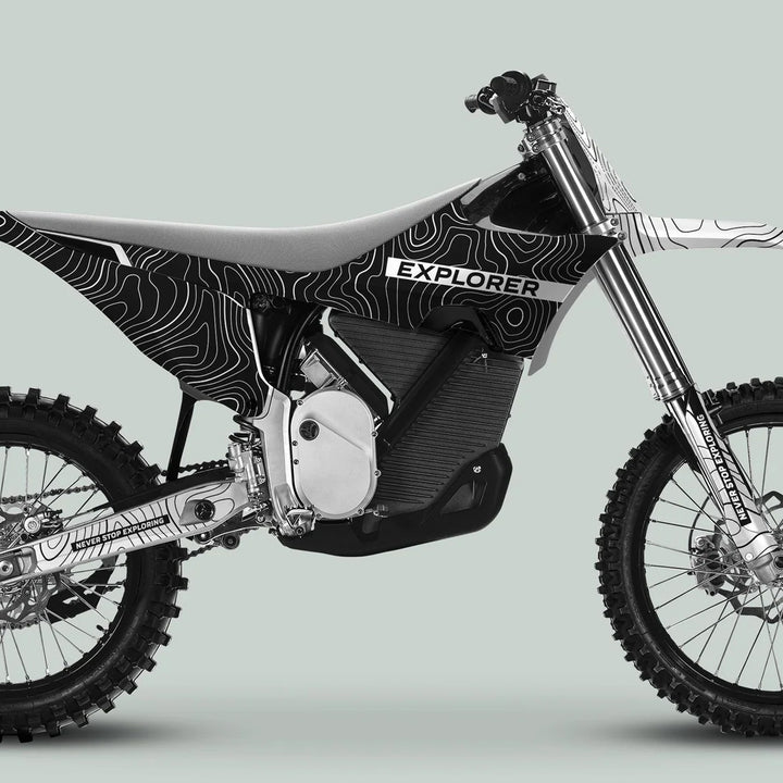 Side-profile of a dirt bike with Stark Varg Graphics Kit EXPLORER BLACK WHITE Decals, showcasing topographic-map graphics and Never Stop Exploring text on swingarm and fork guard.