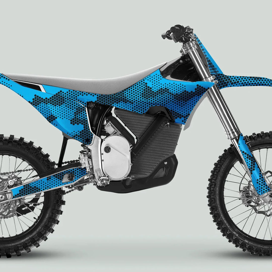 Side profile of a motocross bike with Stark Varg Graphics Kit HEXOCAM CYAN decals, featuring blue hex-dot camo, knobby tires, and electric-bike power unit.