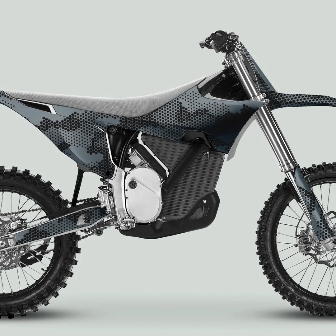 Side-profile of a dirt bike featuring the Stark Varg Graphics Kit HEXOCAM GREY Decals, showcasing a unique hex-camouflage pattern on body panels with knobby tires and skid plate.