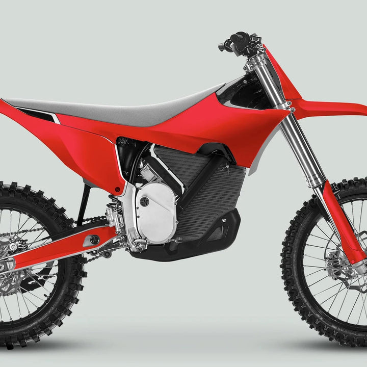 Side-view of a red off-road motorcycle featuring Stark Varg Graphics Kit SOLID COLOR RED Stickers, showcasing knobby tires, long-travel forks, and a sleek seat.
