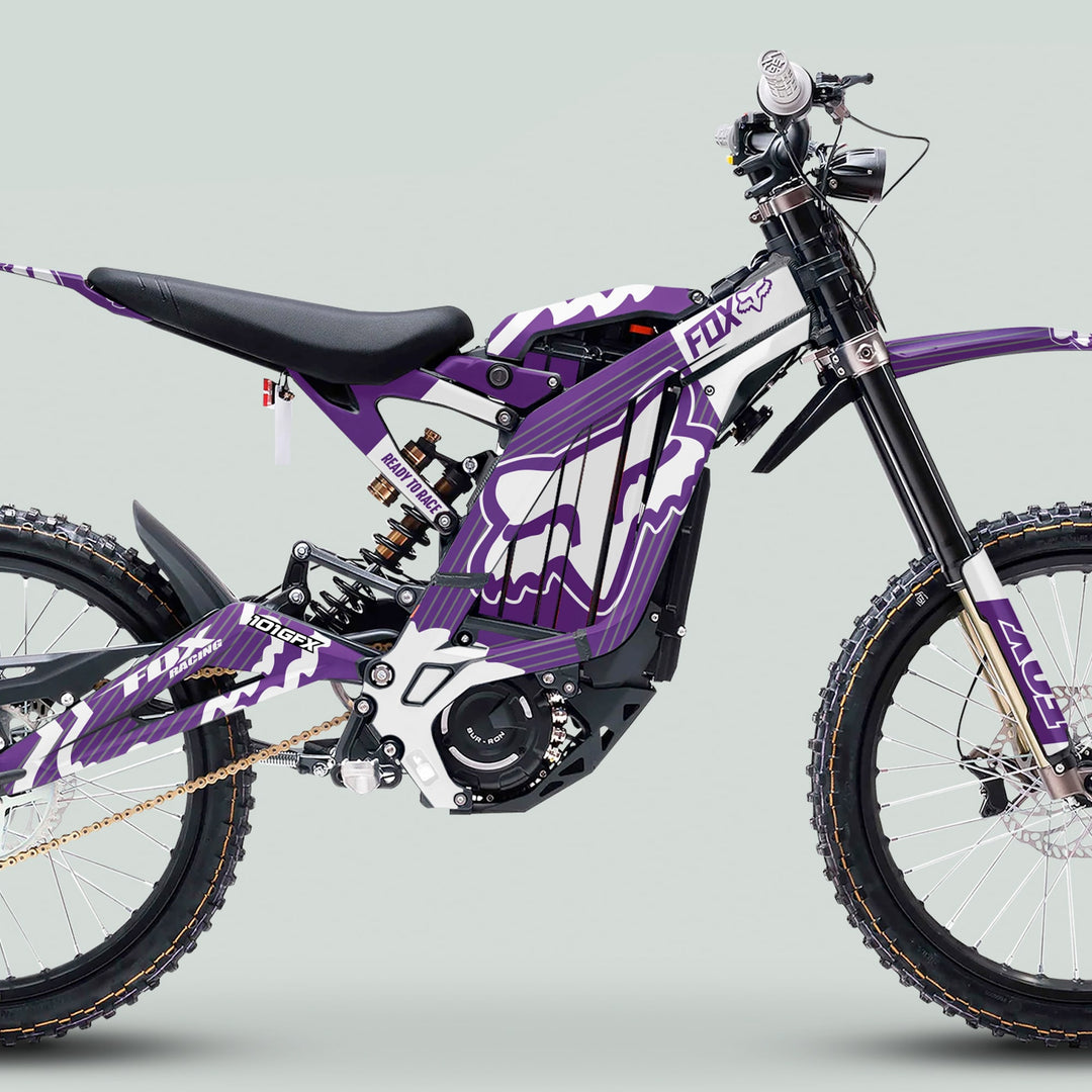 Surron Light Bee X Graphics Kit FOX STRIPES PURPLE White on electric dirt bike with knobby tires, suspension, FOX graphics, and bicycle-style saddle.