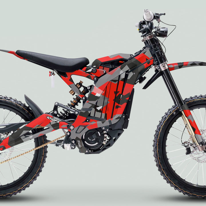 Side-view of the Surron Light Bee X Graphics Kit GEOTECH RED on an electric dirt bike, featuring camouflage-style wrap and knobby tires for rugged terrain.