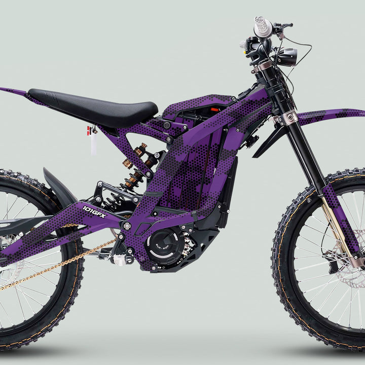 Side-view of a purple Surron Light Bee X Graphics Kit HEXOCAM on an electric motorcycle, showcasing knobby tires, suspension, and motor against a light-gray background.