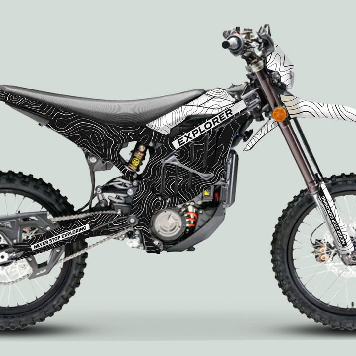 Surron Ultra Bee Graphics Kit EXPLORER BLACK WHITE on a dirt-bike style e-bike, showcasing its contour wrap, chain-drive, and off-road tires, emphasizing durability and style.