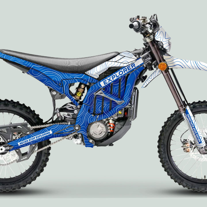 Side-profile of the Surron Ultra Bee Graphics Kit EXPLORER BLUE WHITE on an off-road motorcycle, featuring knobby tires and an electric motor.