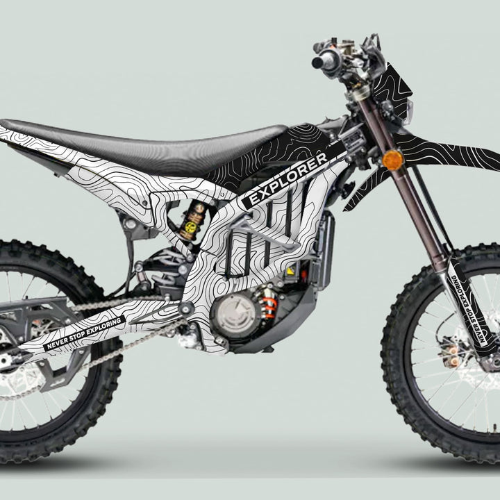 Side view of electric dirt bike with Surron Ultra Bee Graphics Kit EXPLORER WHITE BLACK, featuring topographic-map design, knobby tires, and NEVER STOP EXPLORING slogan.