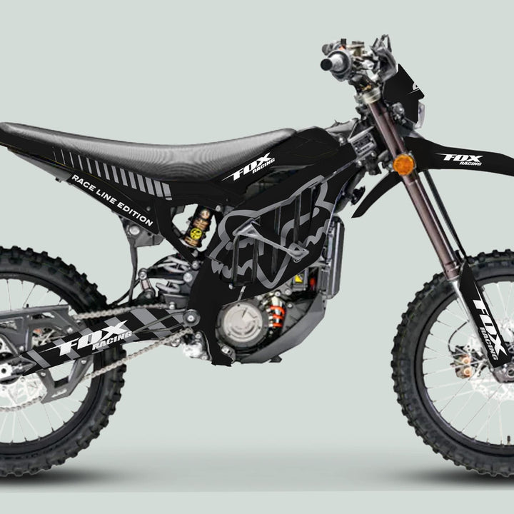 Surron Ultra Bee Graphics Kit FOX RACE LINE Black Grey on motocross bike, showcasing knobby tires, exposed engine, and sleek black/gray Fox-style livery.
