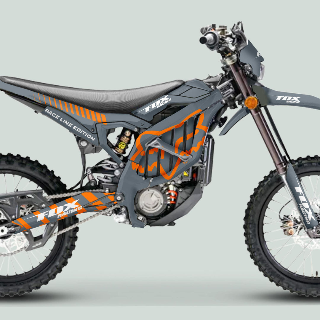 Side-view of a dirt bike with Surron Ultra Bee Graphics Kit FOX RACE LINE Grey Orange, showcasing knobby tires, orange logos, and durable frame enhancements.