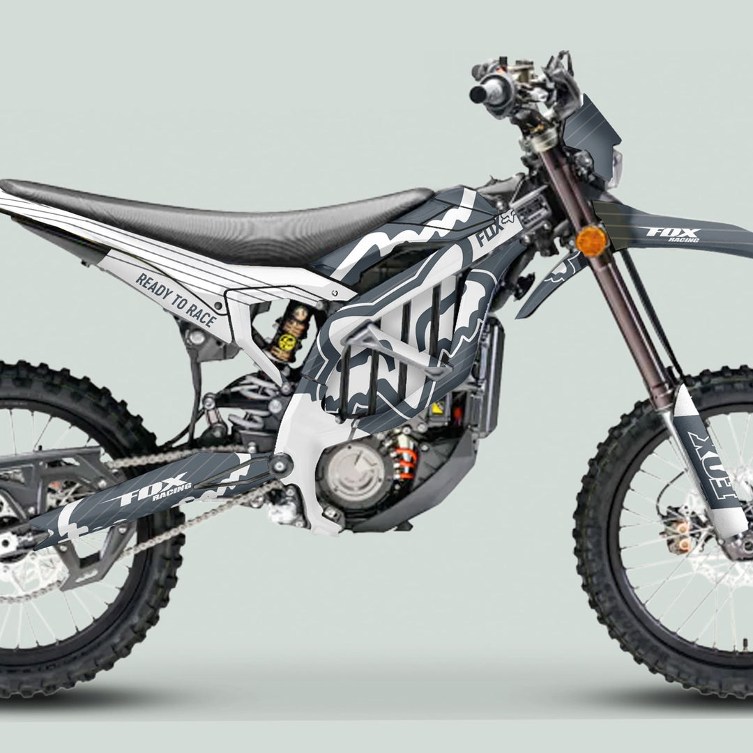 Side profile of Surron Ultra Bee Graphics Kit FOX STRIPES Grey White on a motocross bike, showcasing distinctive Fox Racing graphics and knobby tires.