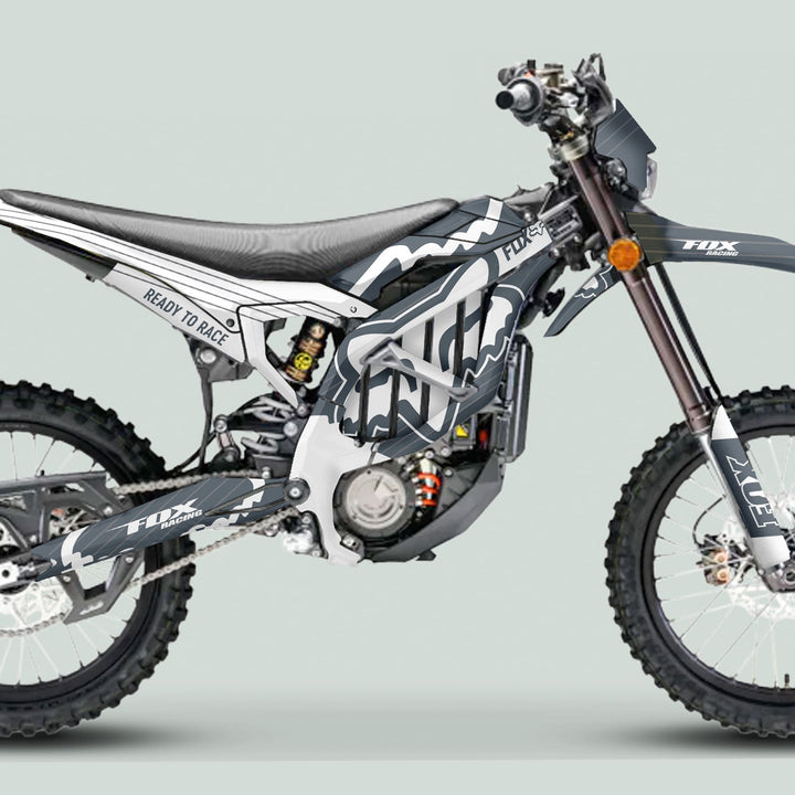 Side profile of Surron Ultra Bee Graphics Kit FOX STRIPES Grey White on a motocross bike, showcasing distinctive Fox Racing graphics and knobby tires.
