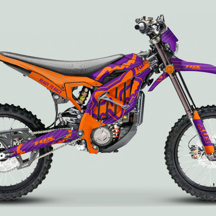 Surron Ultra Bee Graphics Kit FOX STRIPES Purple Orange on dirt bike, showcasing vibrant Fox Racing graphics with knobby tires and matching frame elements.