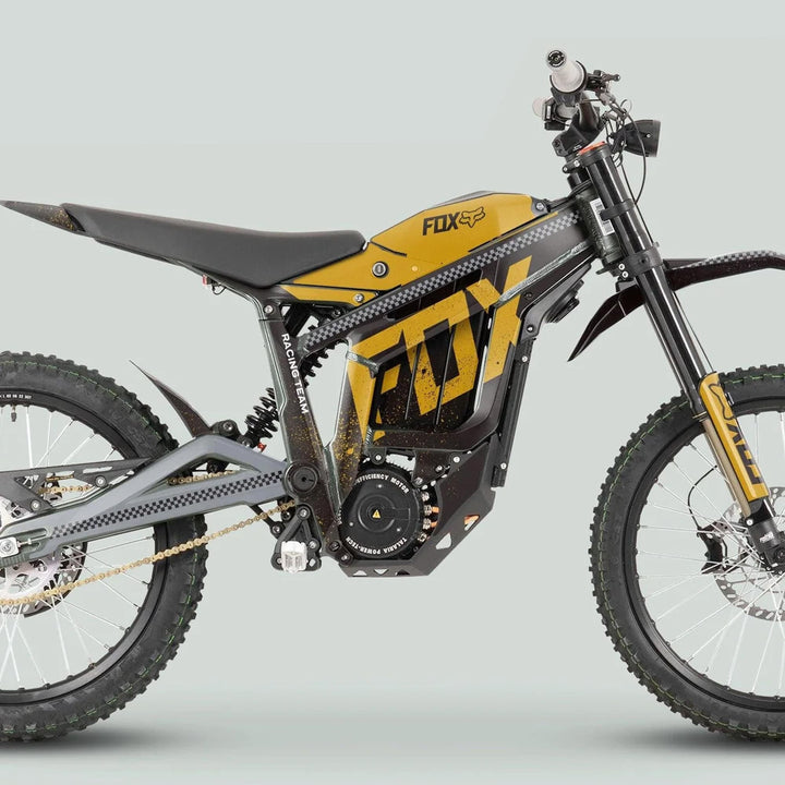 Side profile of an off-road electric motorcycle featuring the Talaria Sting MX3 MX4 Graphics Kit in black gold, co-branded with Fox Racing, showcasing knobby tires and suspension.