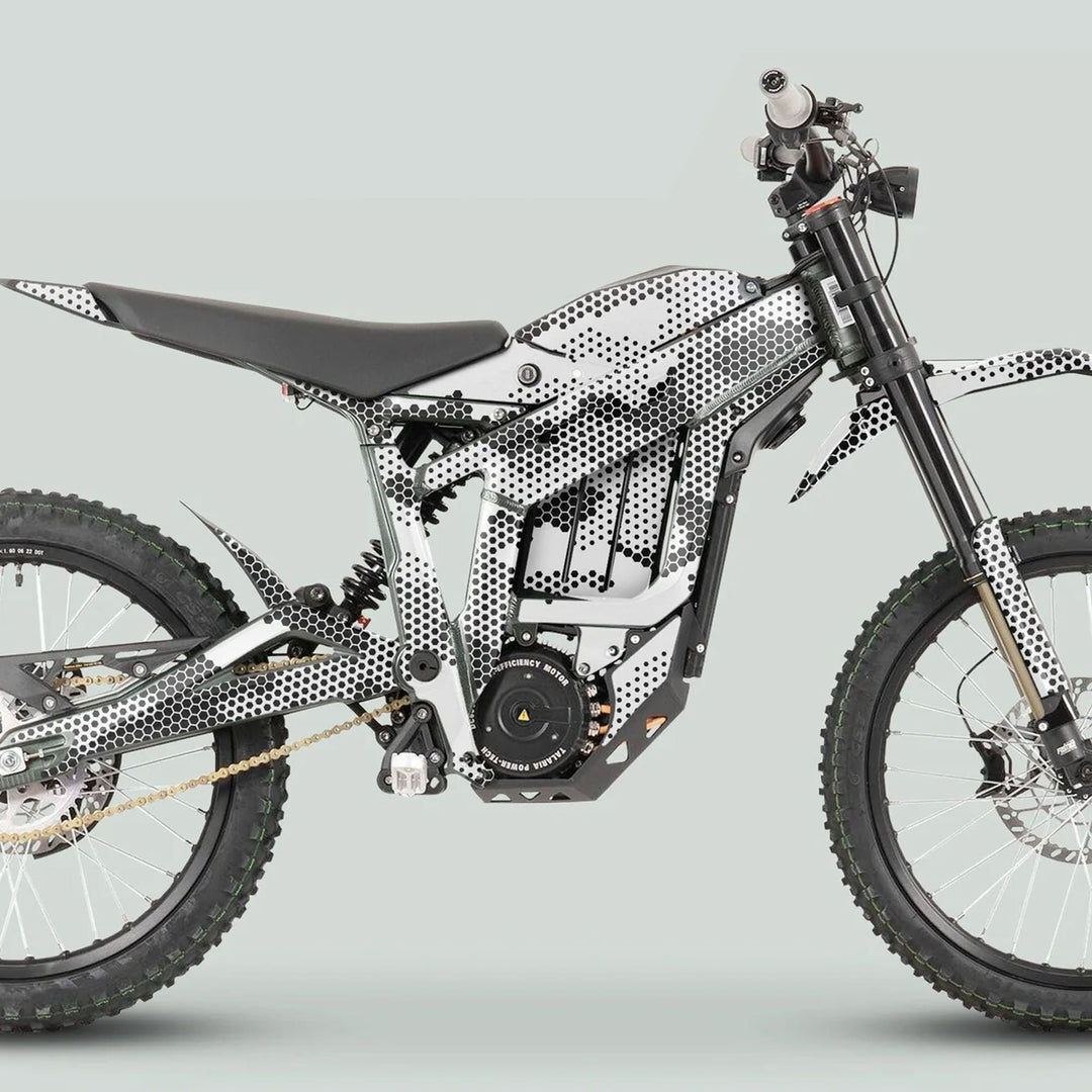 Side profile of an electric dirt bike with Talaria Sting MX3 MX4 Graphics Kit HEXOCAM White, featuring knobby wheels, long-travel suspension, and camo-style wrap.
