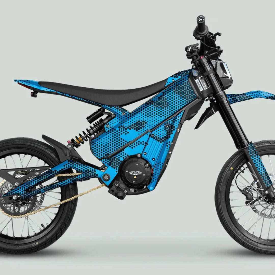 Side-profile of an e-dirtbike with Talaria XXX Graphics Kit HEXOCAM Cyan, showcasing blue honeycomb graphics on frame, central motor, battery, and rugged wheels.